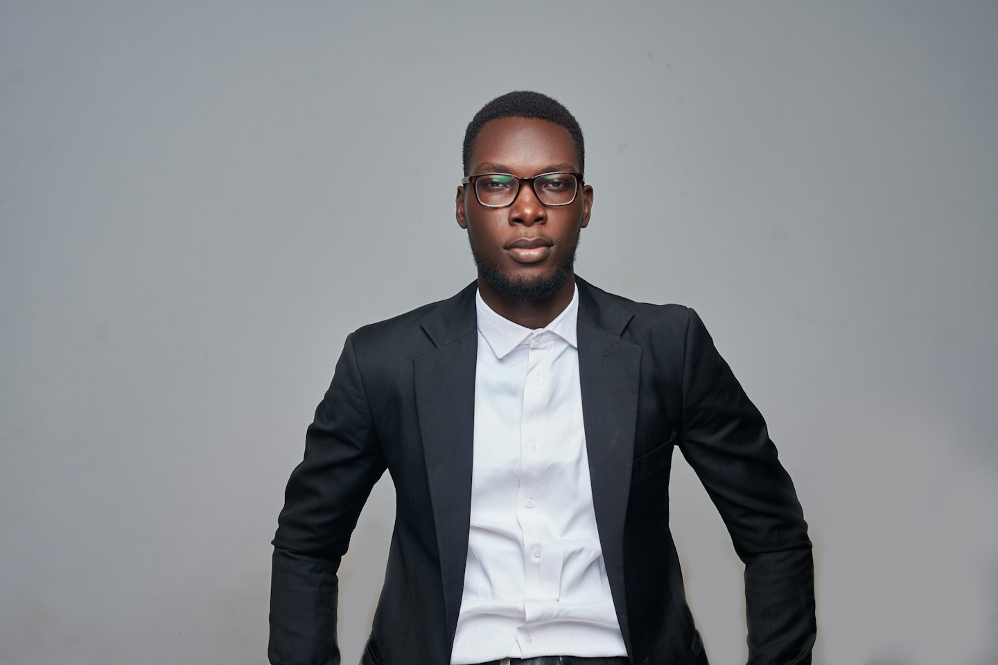 Young Black man in a suit and glasses looking forward.